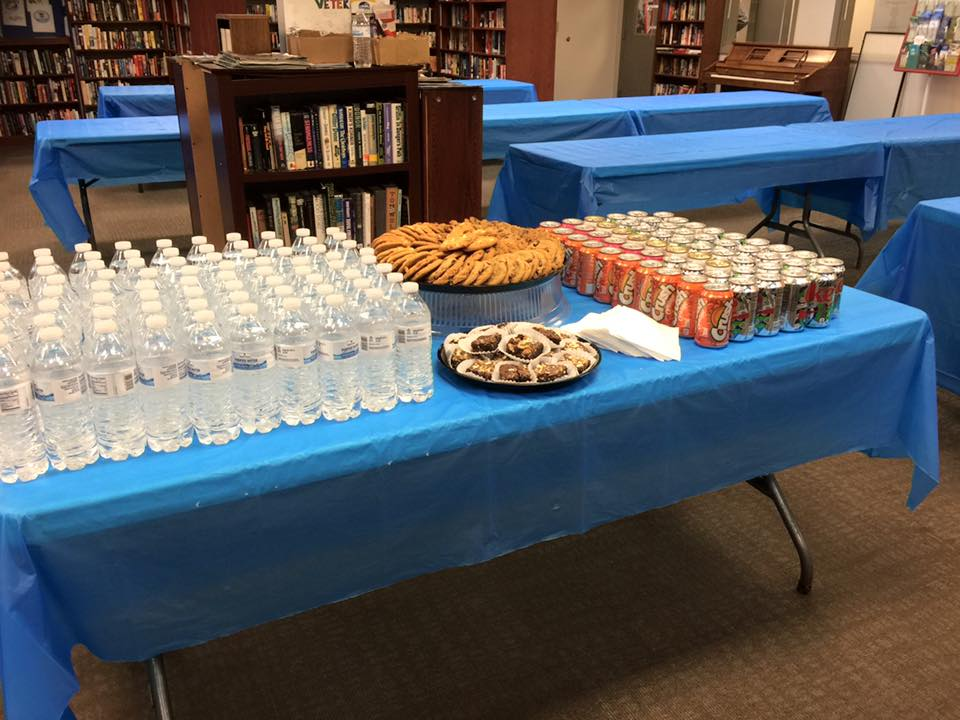 Table full of bottles of water and cans of pop in a library.